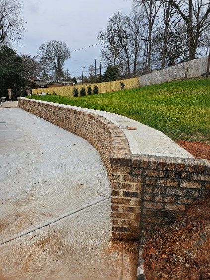 Curved brick retaining wall next to a concrete driveway and grassy hillside.