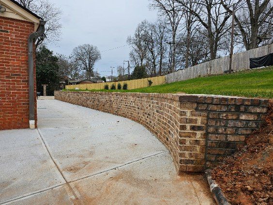 Brick retaining wall curving along a concrete driveway, next to a brick building.