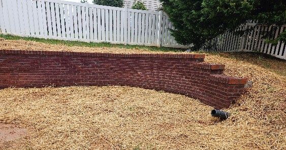 Brick retaining wall with curved steps in a yard, white picket fence in background.