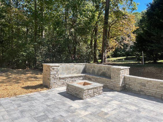Stone patio with built-in seating and fire pit, surrounded by trees.