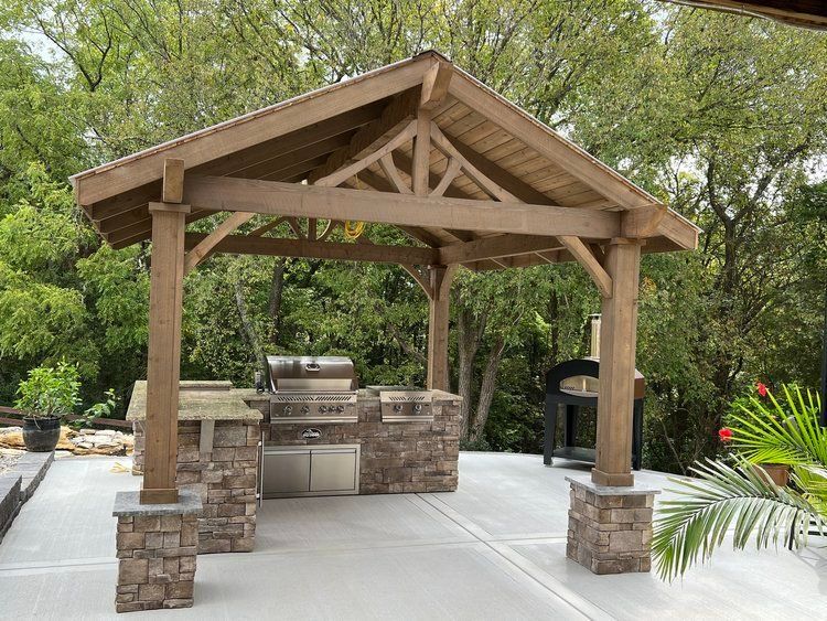 Wooden outdoor kitchen with stone base, grill, and covered area.