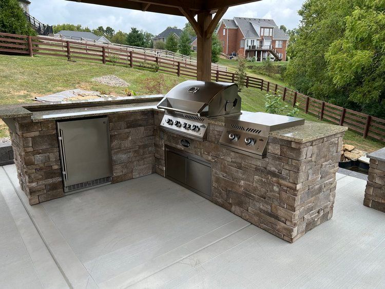 Outdoor kitchen with brick facing, grill, refrigerator, and countertop, under a wooden pergola on a patio.