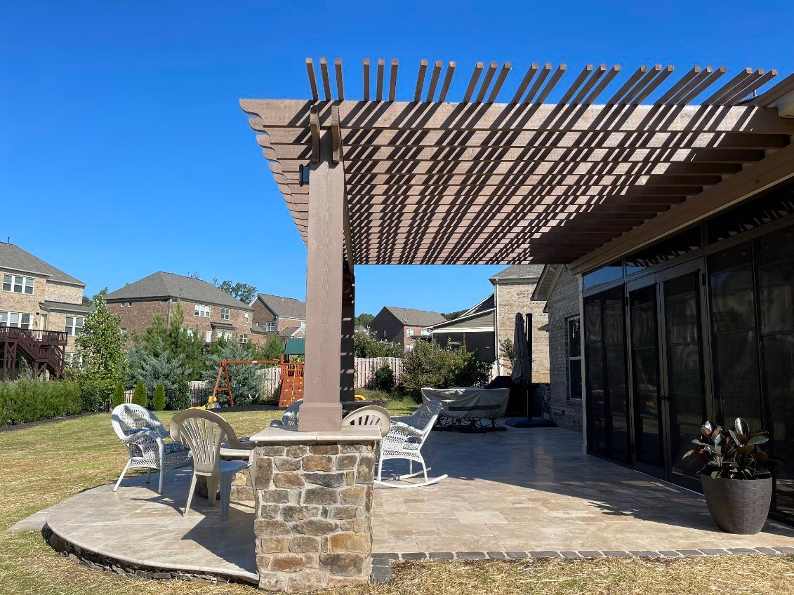 Backyard patio with pergola, stone column, chairs, and shade, blue sky.