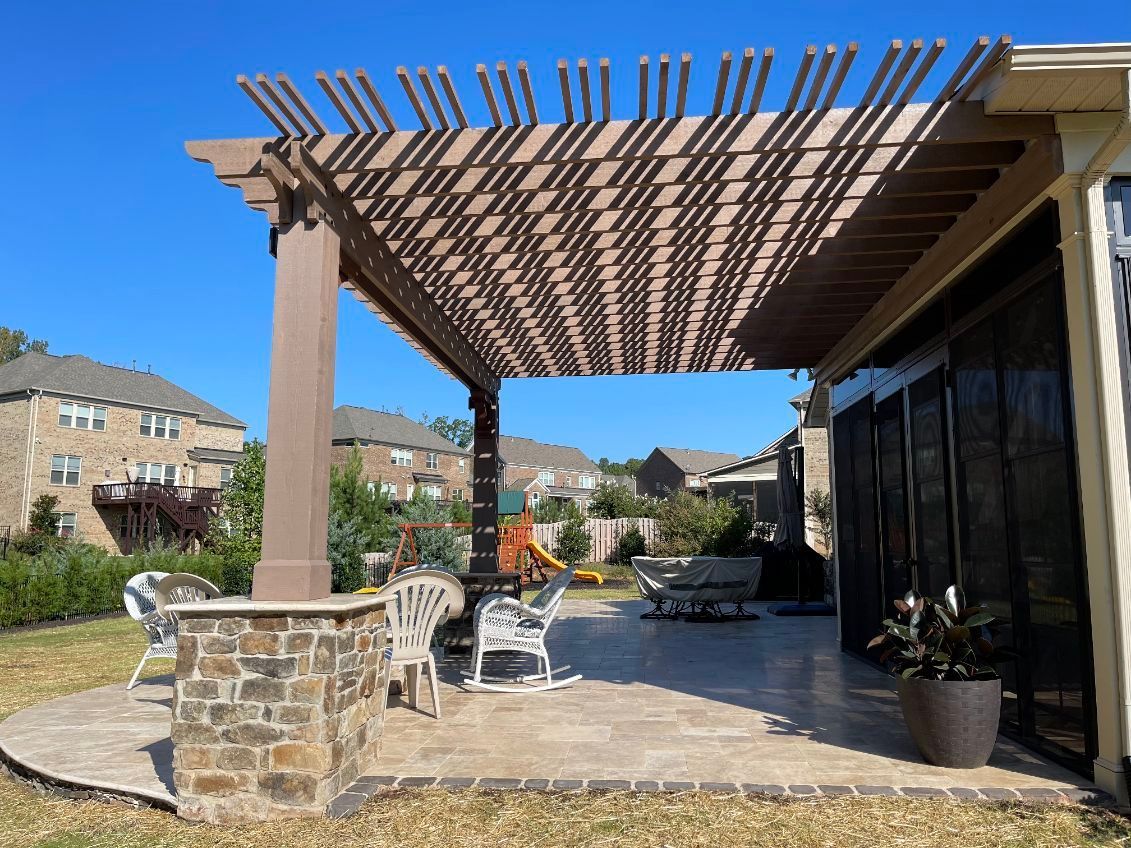 Outdoor patio with a pergola, seating, and fire pit under a blue sky.
