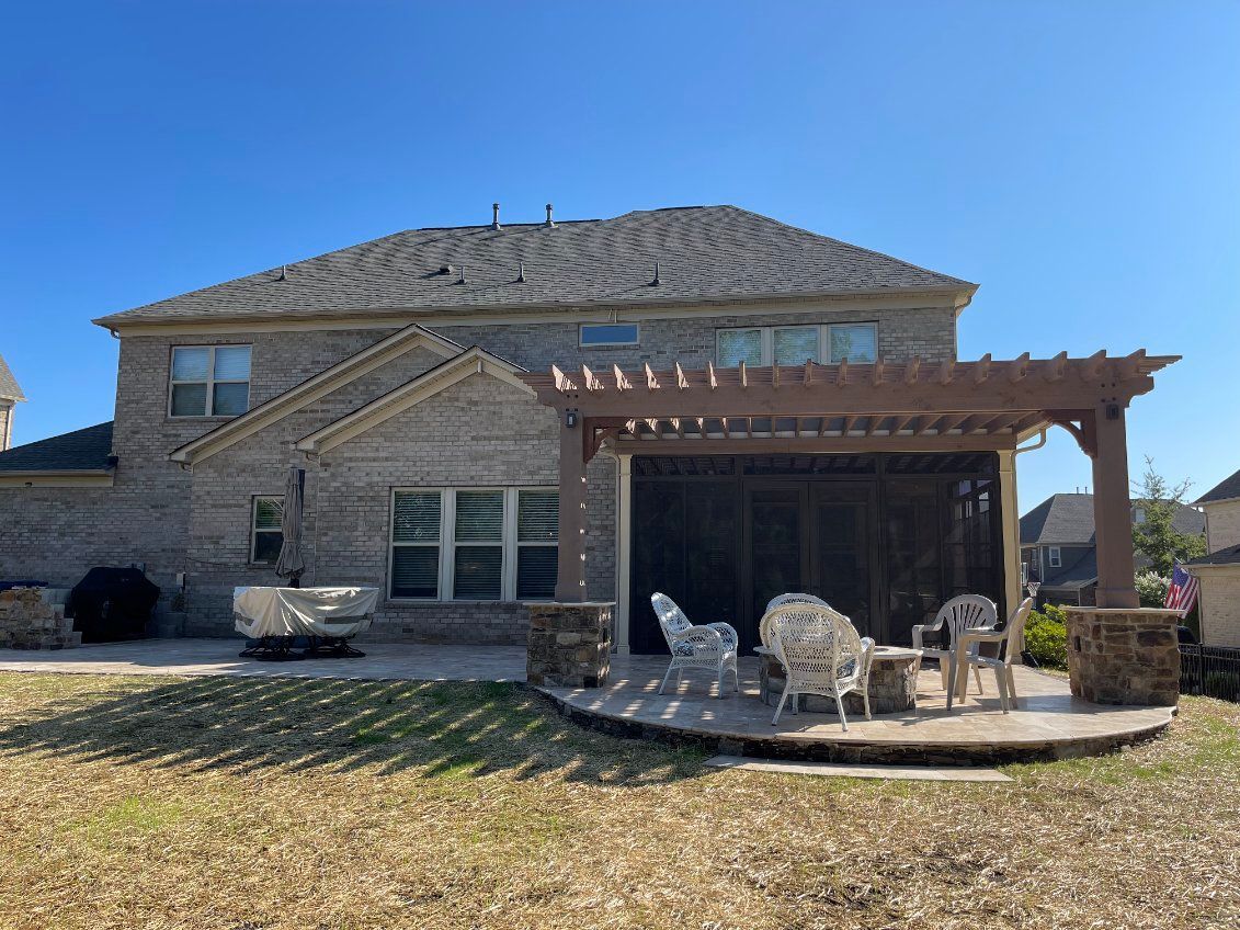 Backyard patio with pergola, seating, and brick home under a clear blue sky.