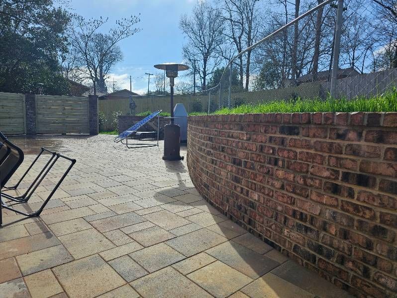 Patio with brick wall, paving stones, outdoor heater, and fencing under a blue sky.
