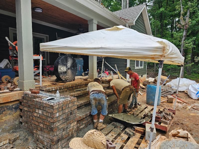 Construction workers building brick steps under a canopy. Outdoor setting with a house.