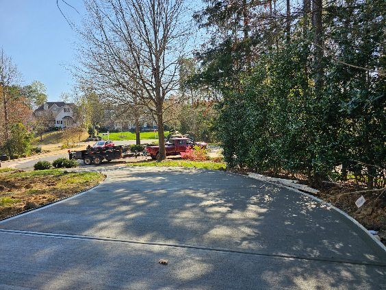 Asphalt driveway leads to parked cars and trees under a sunny sky.