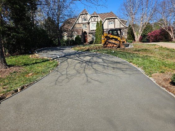 Asphalt driveway leading to a Tudor-style house with a small bulldozer parked on the right.