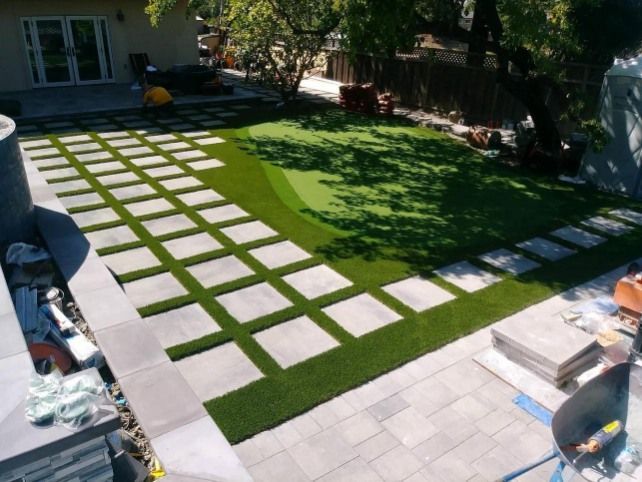 Outdoor patio with square pavers and artificial turf, leading to a grassy lawn.