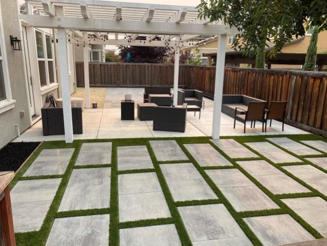 Patio with pergola, outdoor furniture on concrete, and stone pavers with artificial grass.