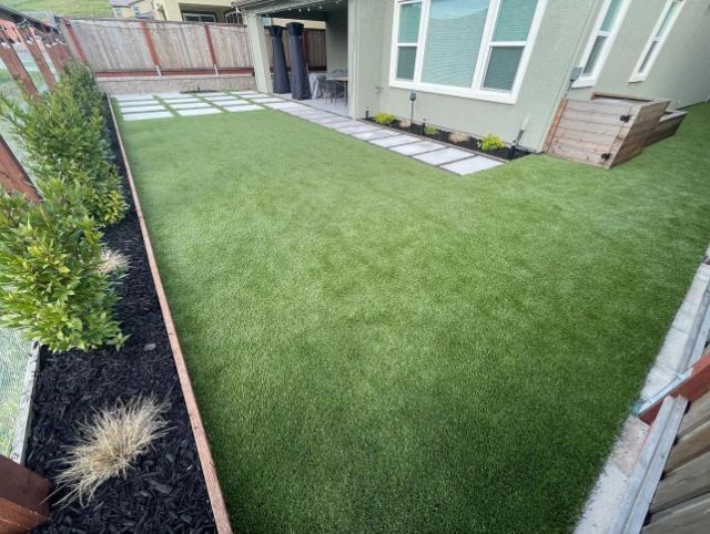 Backyard with green artificial turf, stone patio, and wooden borders.
