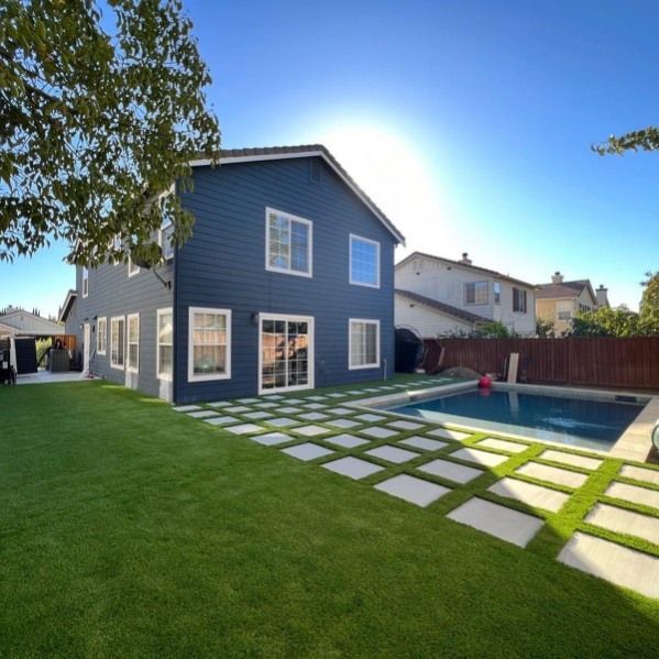 Two-story blue house with a pool in the backyard, stone pavers on lawn, sunny day.