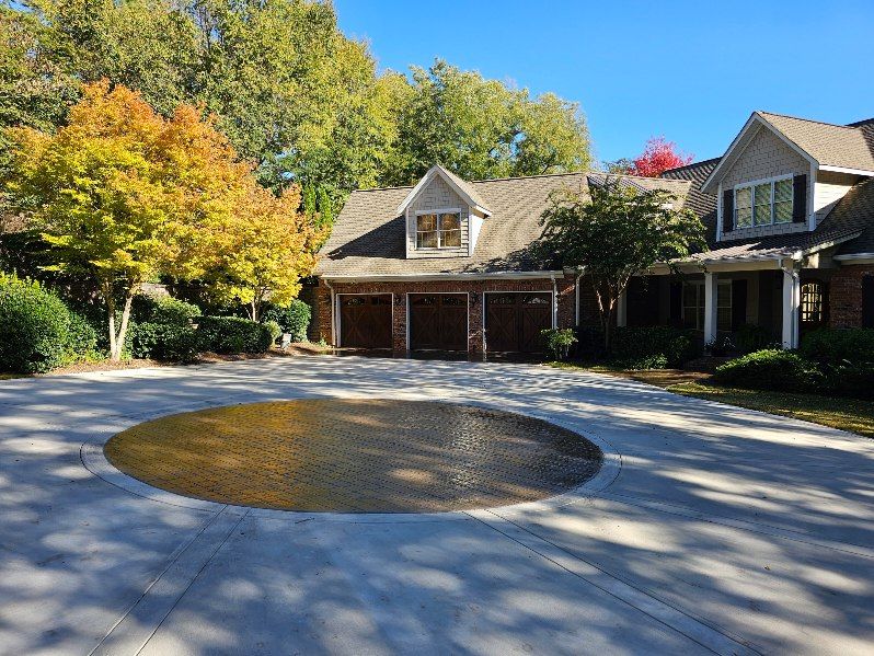 A house with a three-car garage and circular driveway. Autumn trees in the background, blue sky.
