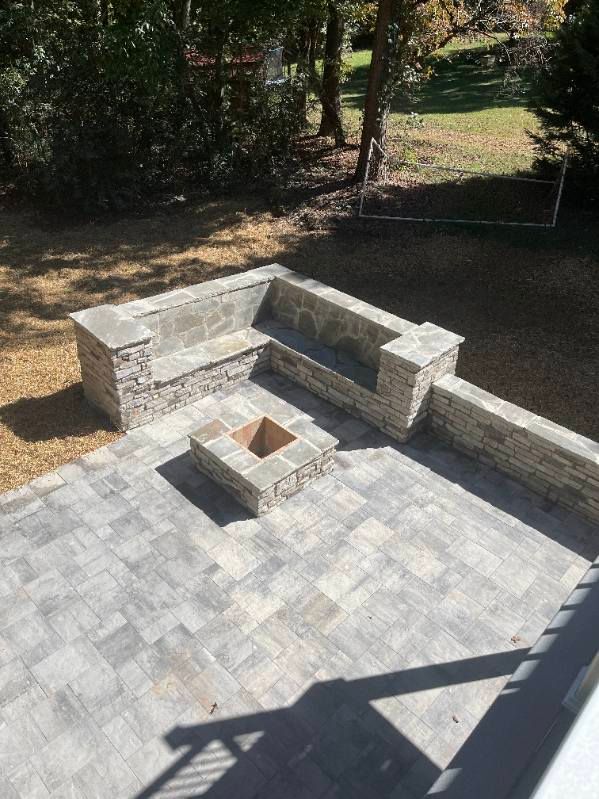 Stone patio with built-in seating around a fire pit. Gray pavers and beige stone walls, outdoor setting.