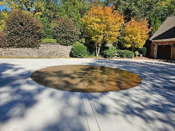 Circular, grassy area within a concrete driveway, with colorful autumn trees in the background.