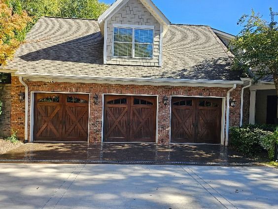 Three dark wood garage doors with brick accents under a brown shingle roof.