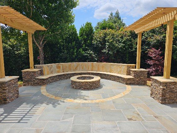 Outdoor seating area with a stone fire pit, benches, and wooden pergolas.