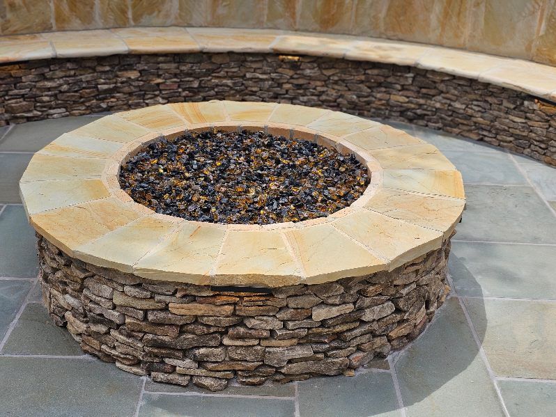 Stone fire pit with curved stone seating on a paved patio.