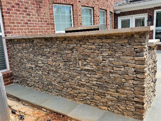 Stone-clad outdoor kitchen counter with built-in grill, set against a brick building.