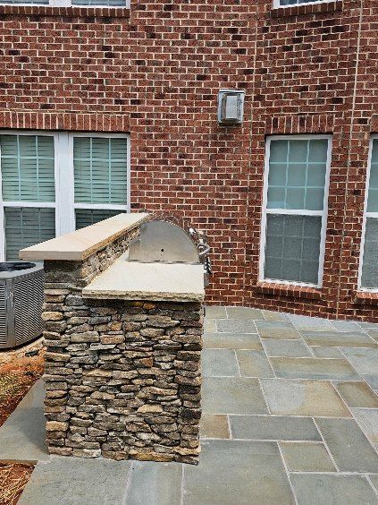 Outdoor grill built with stacked stone and concrete countertops, set against a red brick wall.
