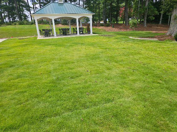 Green lawn with gazebo and trees in the background.