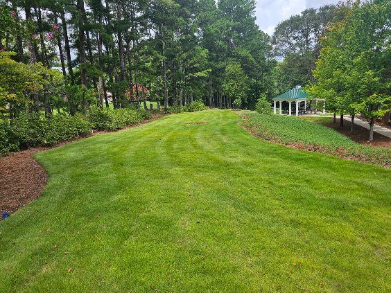 Green lawn with a slight slope, trees, and a gazebo in the distance.