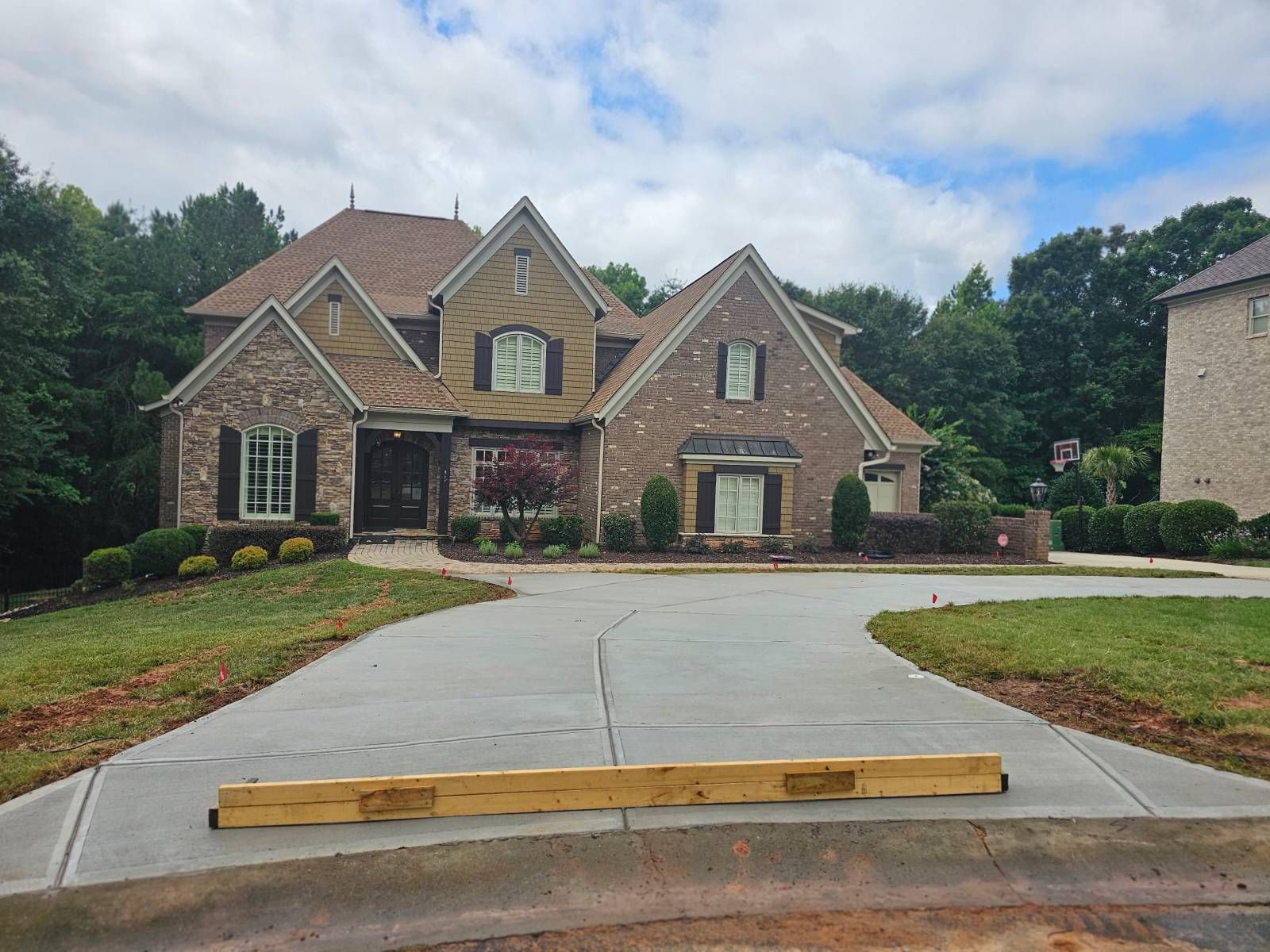 House with brick facade, brown roof, and concrete driveway on a cloudy day.
