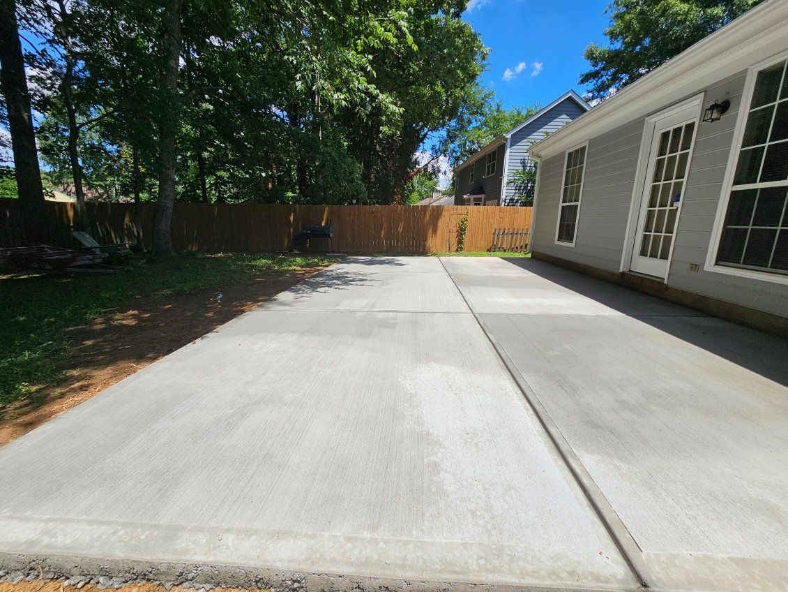 Concrete patio with a gray house and a wooden fence in the background.