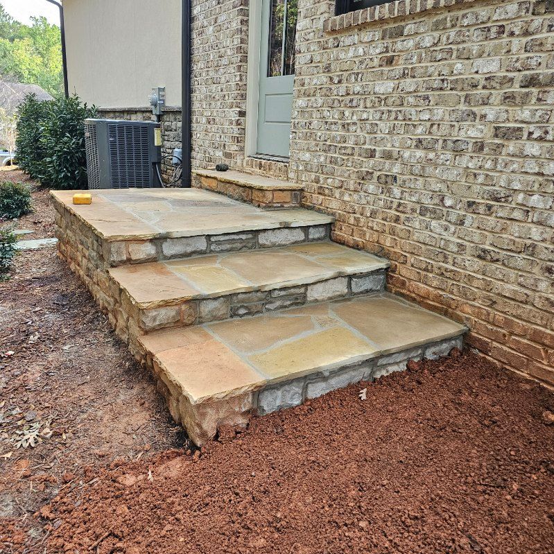 Stone steps leading up to a brick building's doorway. Ground is dirt/mulch.