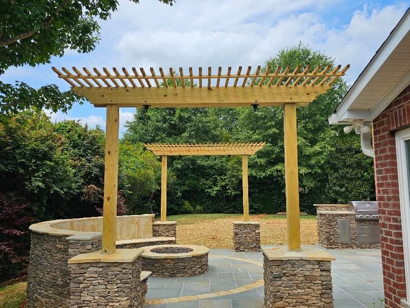 Wooden pergola structure in a backyard patio area with stone features and trees.