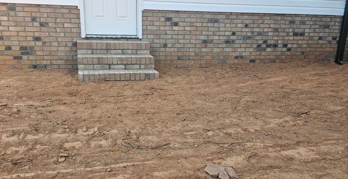 Brown, dead grass in front of a brick house with steps leading to a white door.