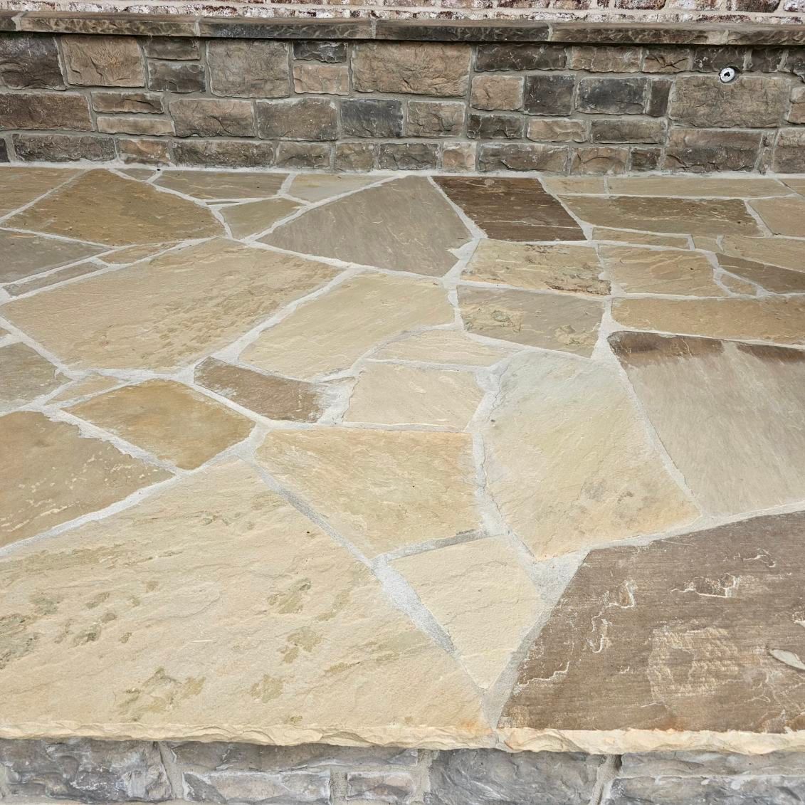Tan and brown flagstone patio with a brick border.