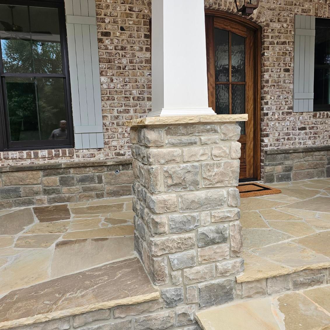 Exterior of a house with stone accents, a white column, brick wall, wood door, and stone patio.