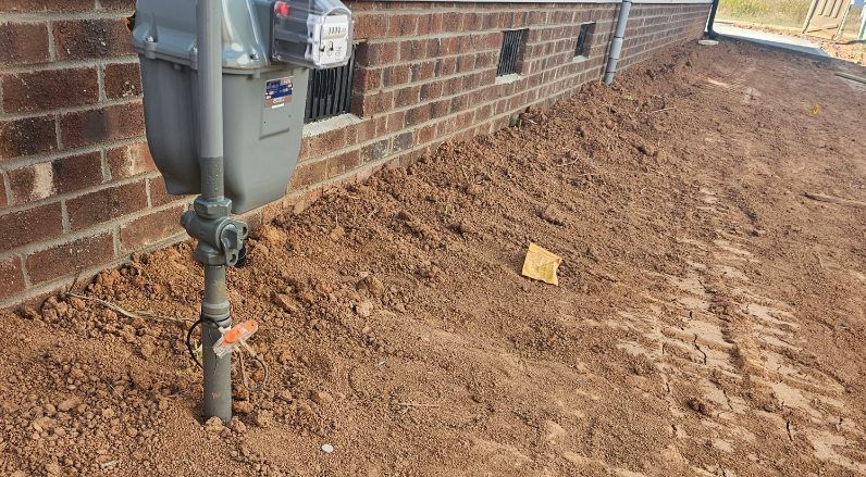 Gas meter on a brick building with dirt ground.