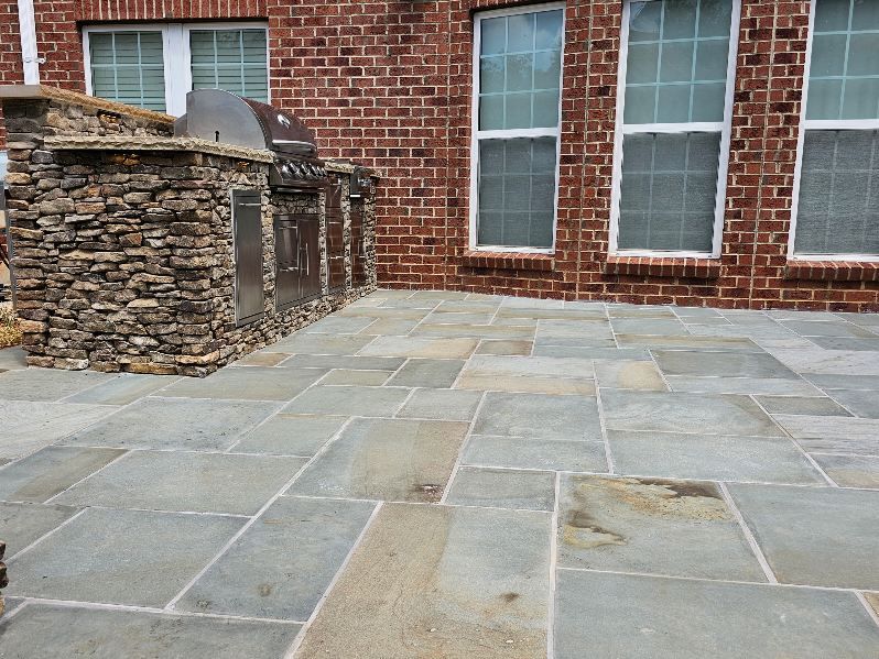 Outdoor patio with stone pavers, brick wall, and built-in grill area.