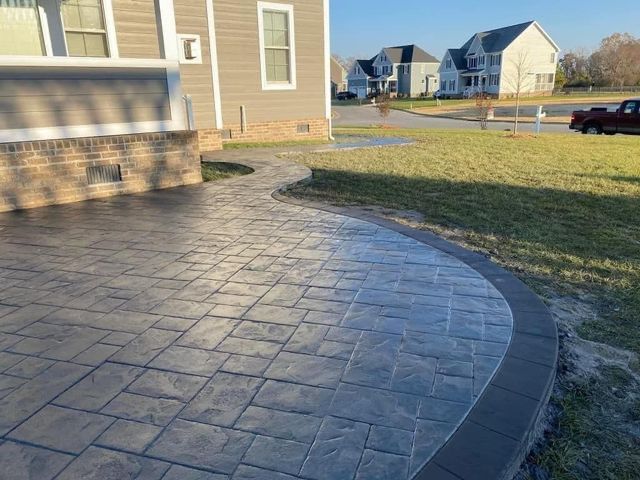 Stamped concrete patio with a dark grey stone pattern. Edge of yard with grass and houses in the background.
