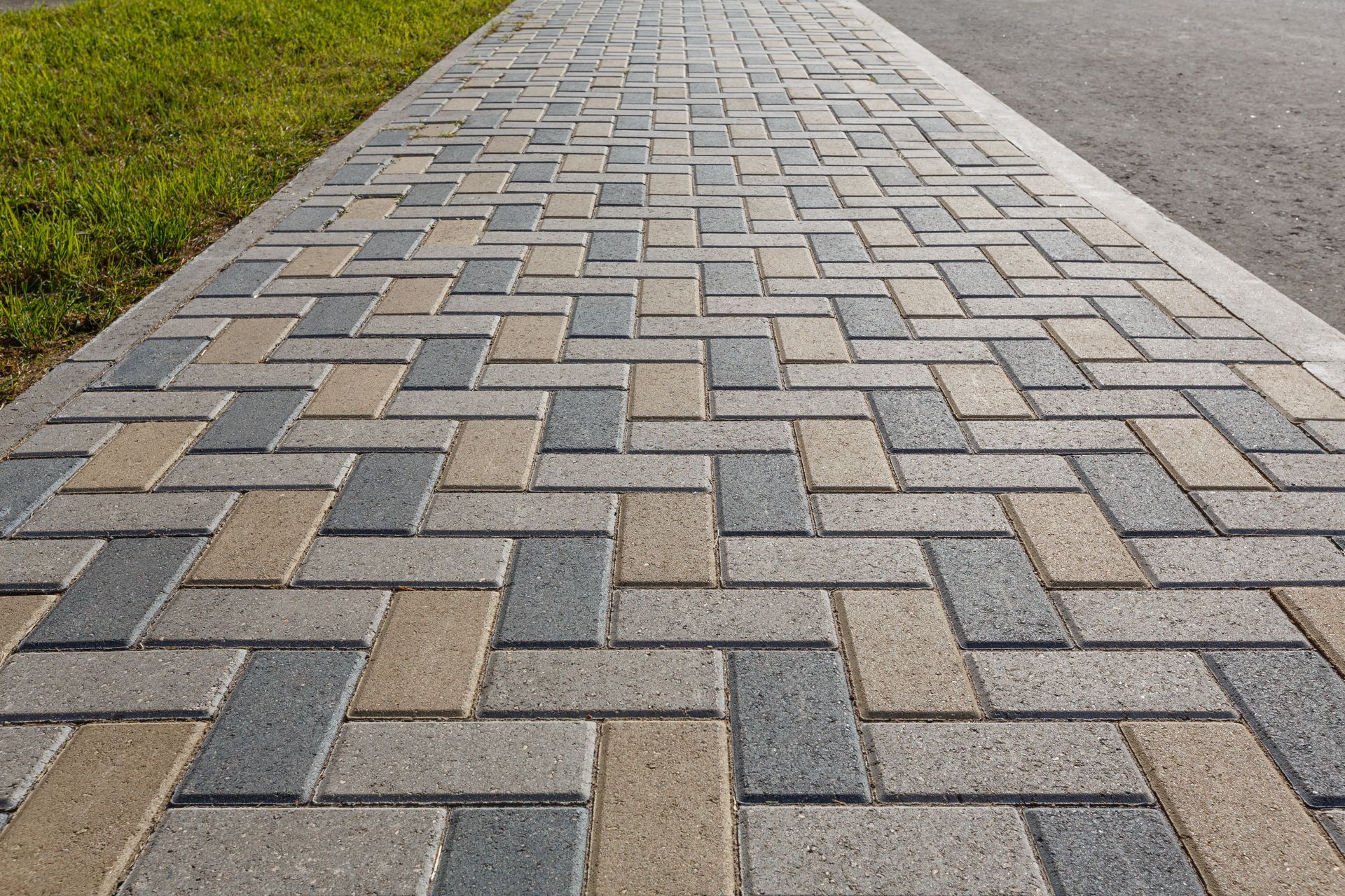 Brick walkway with herringbone pattern, bordered by grass and asphalt.