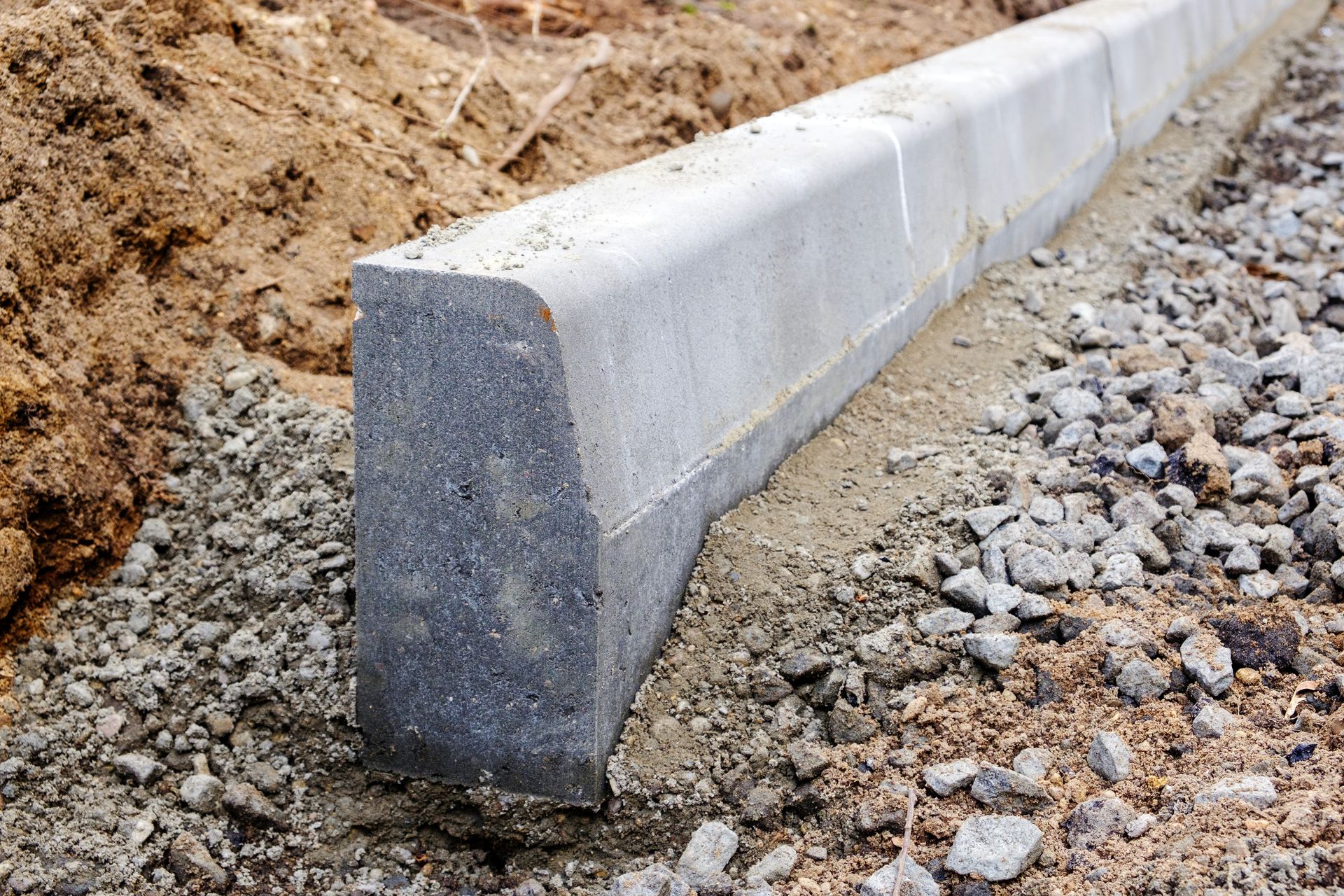 Concrete curb being installed on a gravel base next to soil.