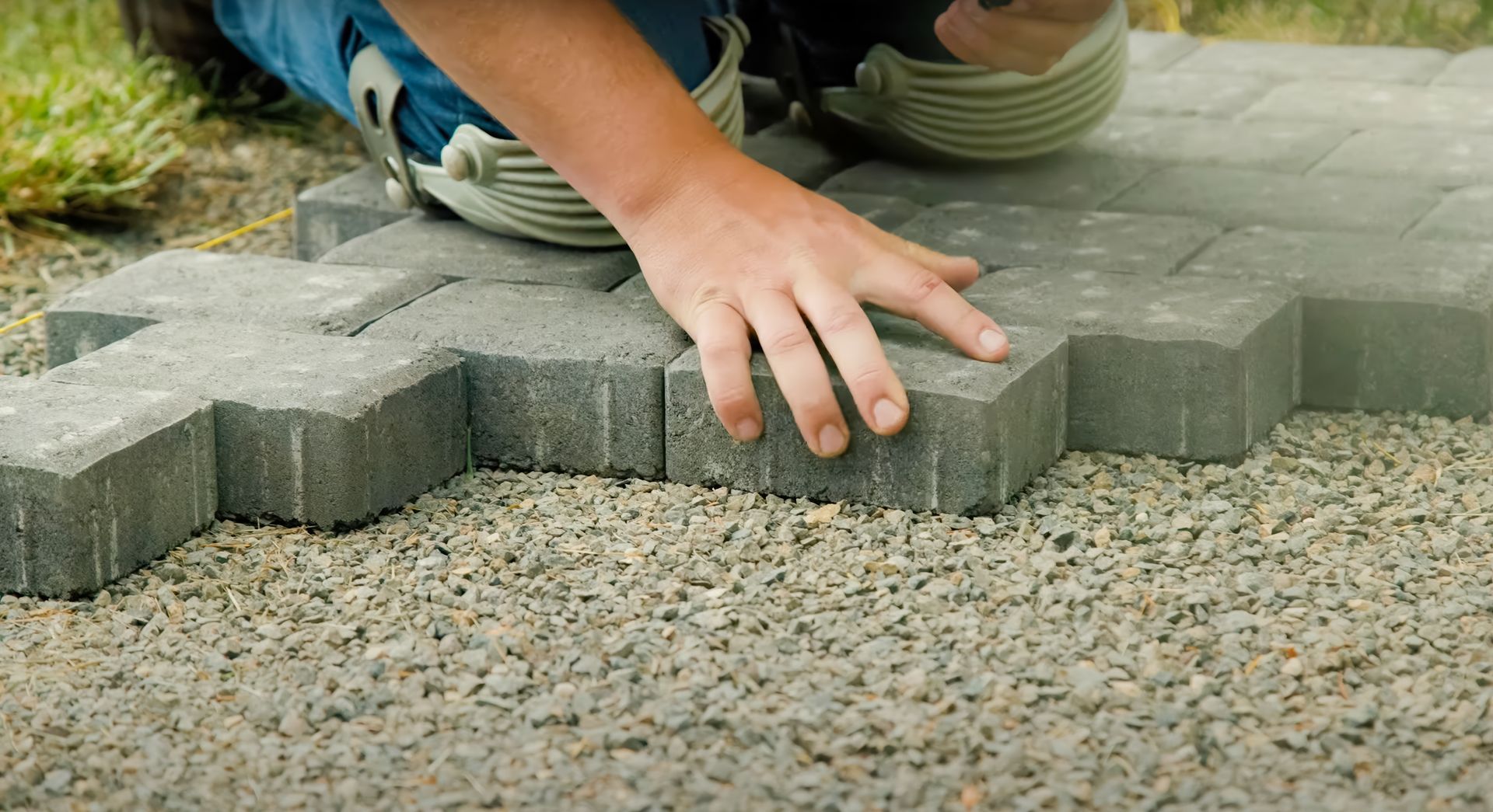 Person installing gray interlocking pavers on gravel base.