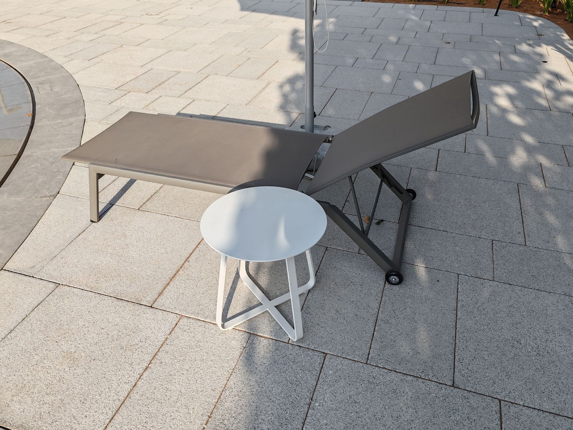 Gray chaise lounge and white side table on a stone patio.