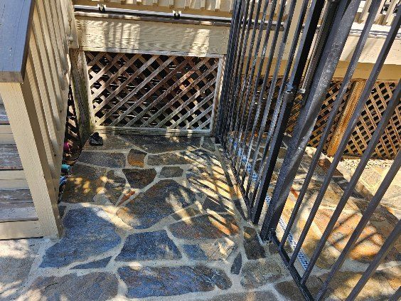 Stone walkway with latticework and black metal gate beneath wooden structure.