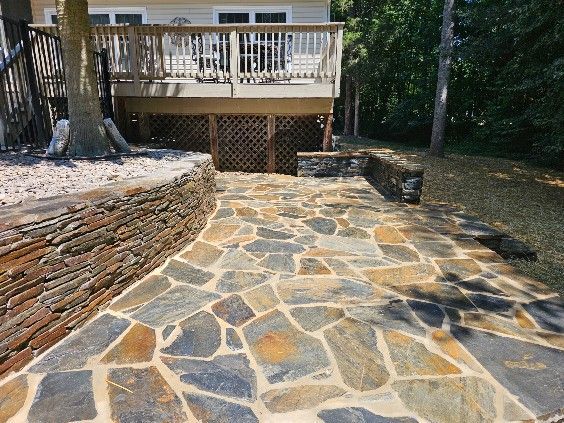 Stone pathway leading to a wooden deck, bordered by stone walls and trees.