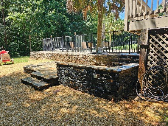 Stone retaining wall and steps with a pool area, palm tree, and grassy yard.