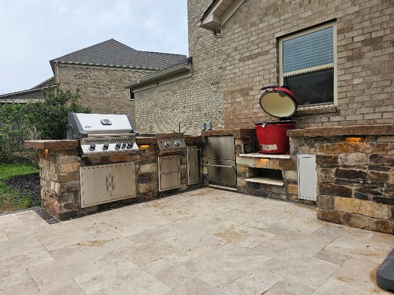 Outdoor kitchen with stone counters, grill, smoker, and storage under a brick home.