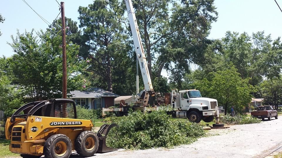 Tree trimming: A truck with a lift and a skid steer removing branches near a house and power lines.