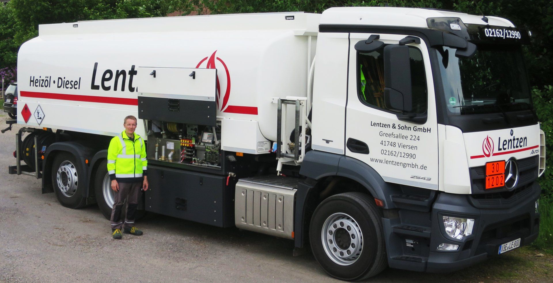 Eine Person in einer neongelben Warnweste steht neben einem weißen Tankwagen mit roter Aufschrift.