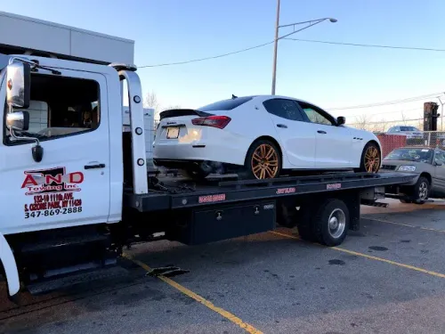 White Maserati sedan on a tow truck, preparing to be transported.