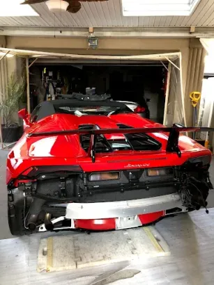 Red Lamborghini with rear bumper removed in a garage.