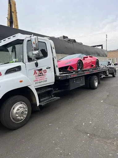 Pink Lamborghini being towed on a flatbed truck.